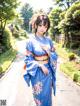 A woman in a blue kimono standing on a sidewalk.