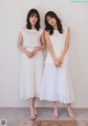 Two women standing next to each other in white dresses.